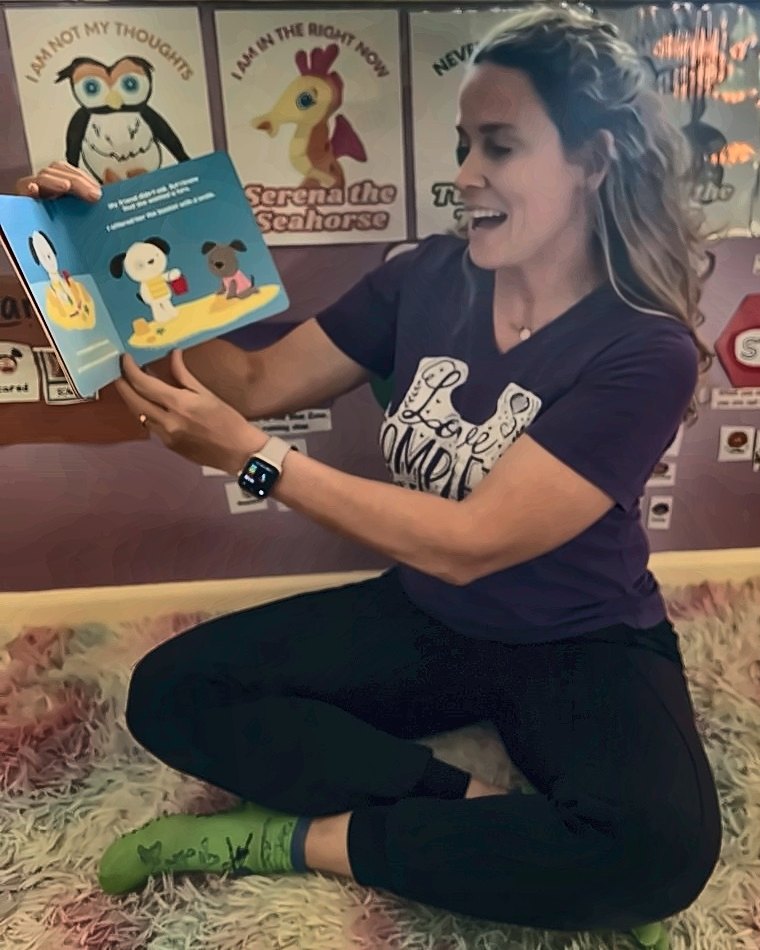 Angela reading a picture book aloud, mid-story, with a big smile