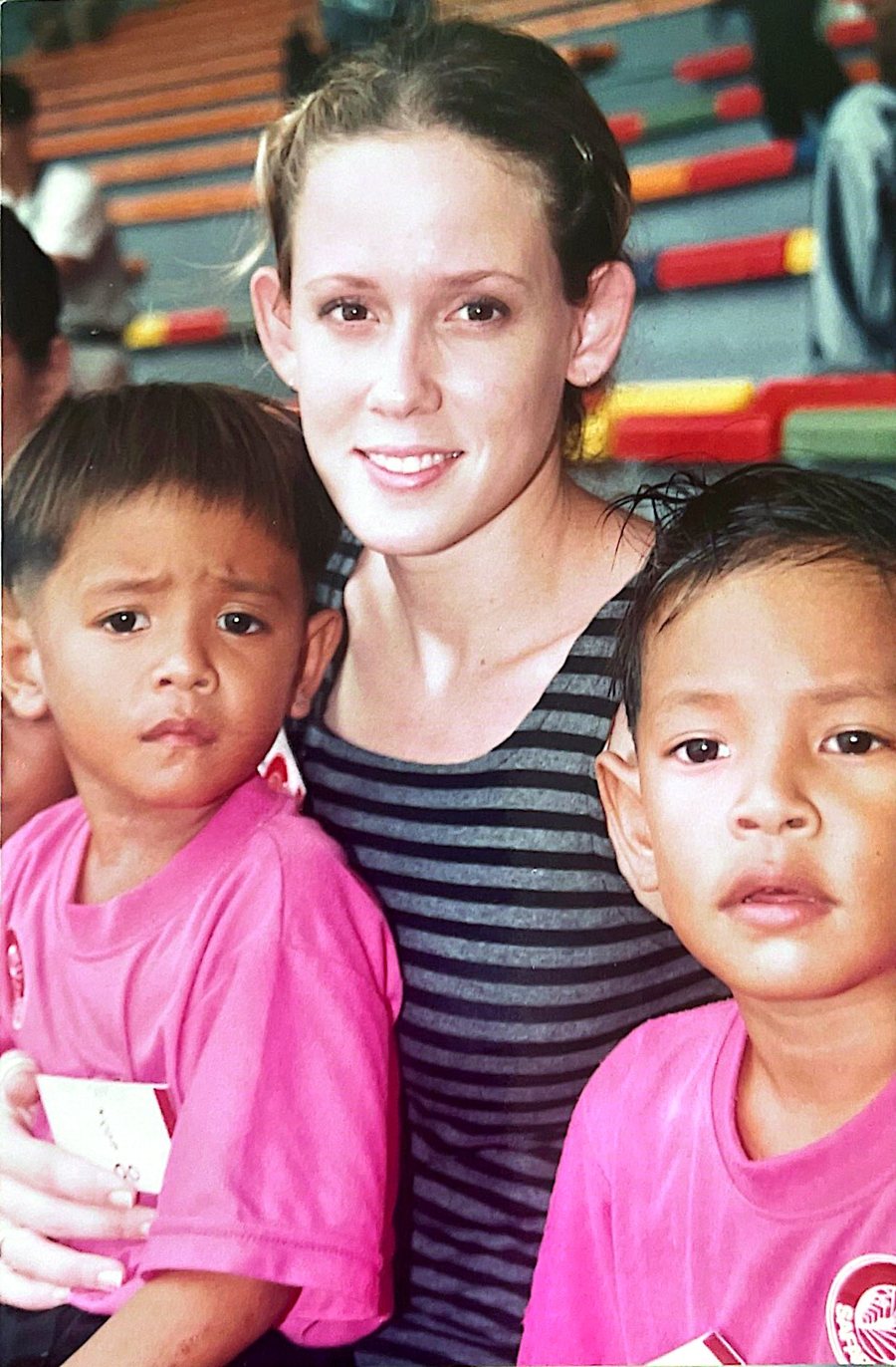 Angela as a young woman in Thailand, sitting with two small boys in pink shirts